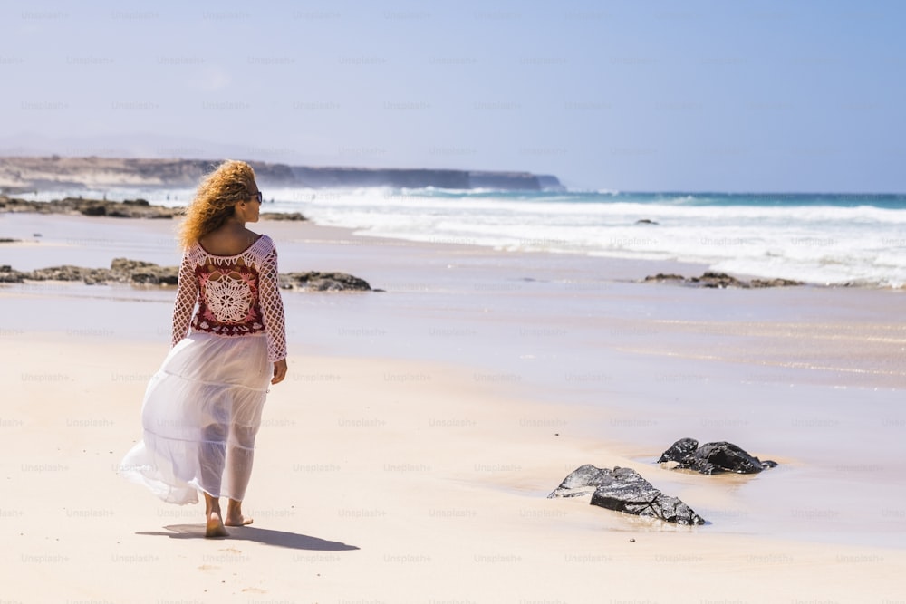Persone libere e vacanze estive per una donna adulta indipendente solitaria in spiaggia che guarda l'orizzonte con l'oceano blu sullo sfondo e il paesaggio panoramico con la sabbia