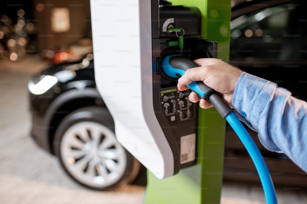 Mann steckt Kabel in die Ladestation für Elektroautos im Autohaus, Nahaufnahme