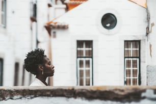 Side view with a shallow depth of field with a selective focus on a beautiful young African female, her face profile is between the stone fence in a defocused foreground and an antique house behind