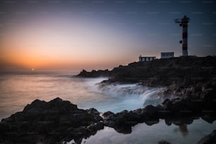 Beautiful sea ocean landscape with big powered waves on the rocks during sunset with classic lighthouse in background -concept of travel and scenic place