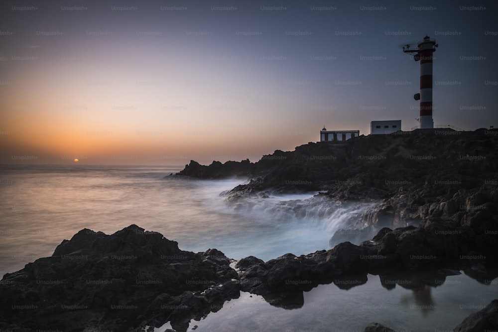 Beautiful sea ocean landscape with big powered waves on the rocks during sunset with classic lighthouse in background -concept of travel and scenic place