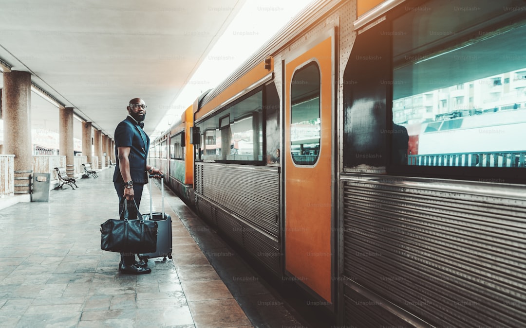 Wide-angle view of an elegant bearded bald mature African man entrepreneur standing with his bags on a railway station p