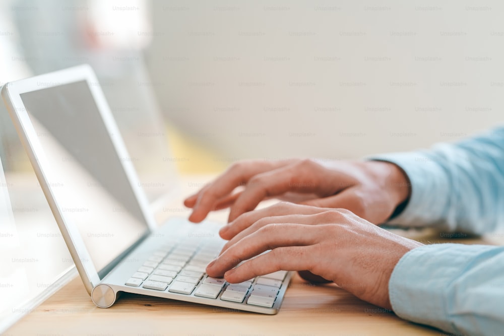 Hände eines jungen Website-Designers, der Tasten der Tastatur berührt, während er vor dem Touchpad am Arbeitsplatz im Büro arbeitet