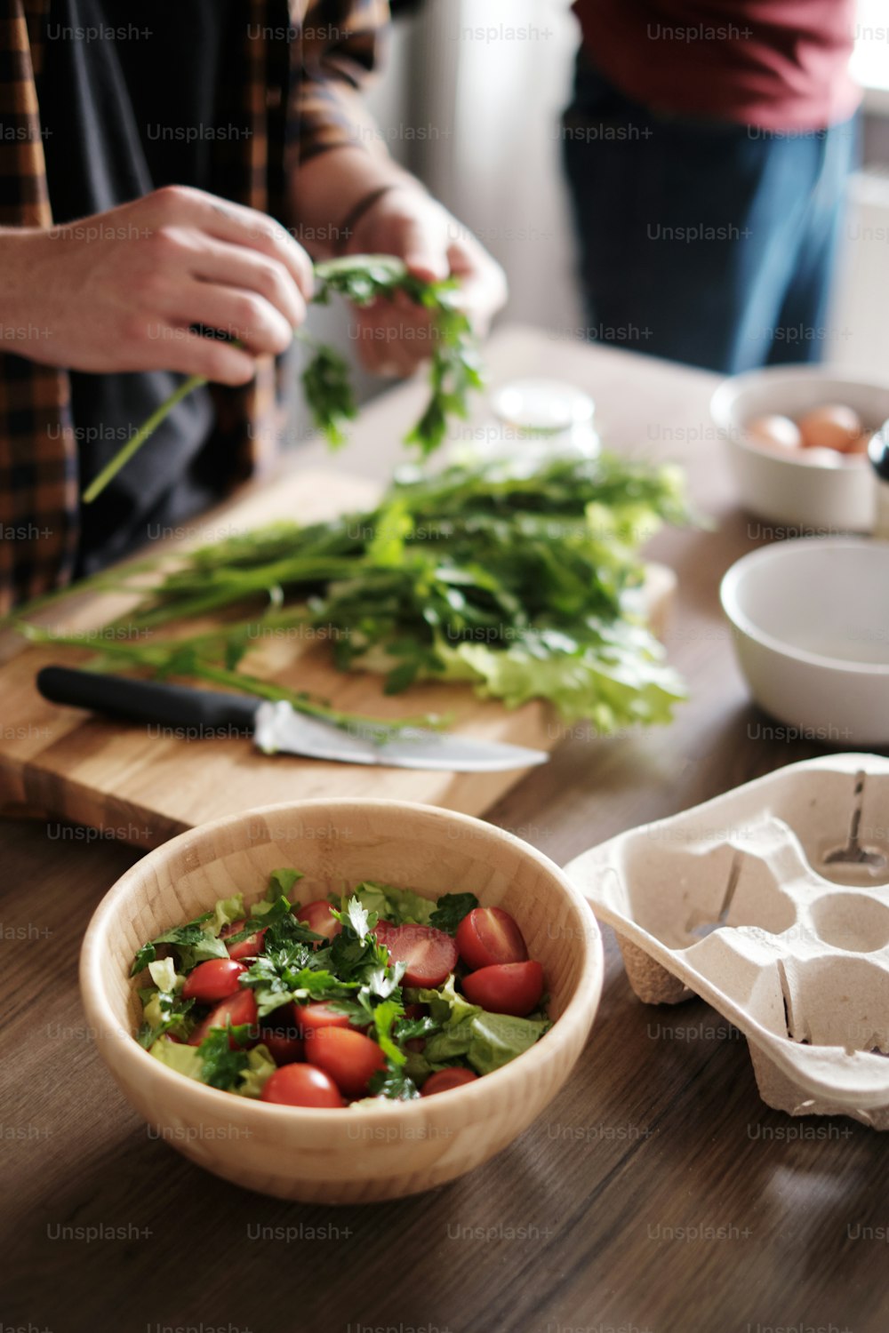 Nahaufnahme von Männerhänden, die grünen Salat in der Küche schneiden und Salat auf Holztisch zubereiten