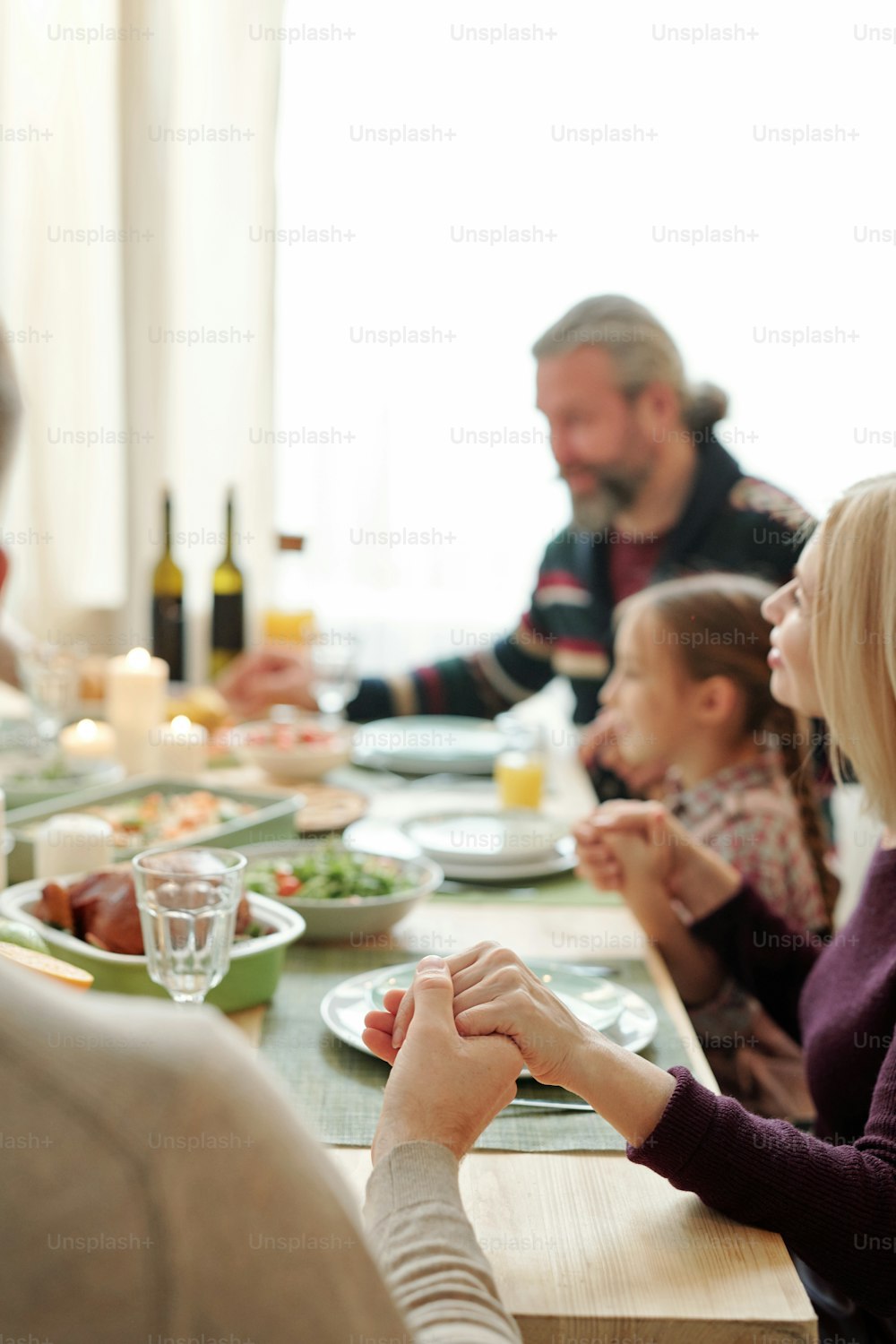 Hombre joven, mujer rubia, su esposo y su pequeña nieta sosteniendo de la mano sobre la mesa festiva durante la oración de Acción de Gracias
