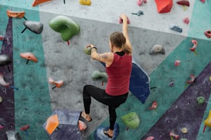 Rear view of young sportswoman in activewear grabbing by small rocks on climbing wall while moving upwards