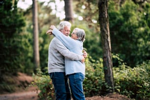 Senior active couple enjoying the outdoor nature forest with hugs and love together - forever life concept with mature man and woman - elderly and beautiful forest green in background