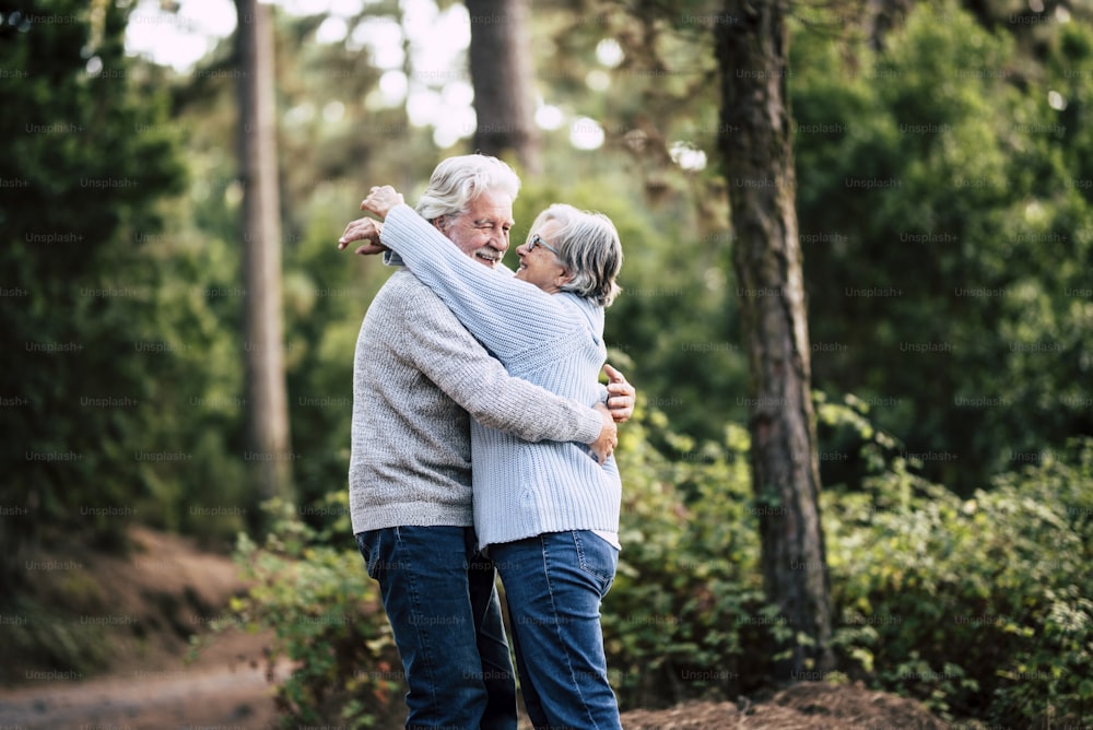Senior active couple enjoying the outdoor nature forest with hugs and love together - forever life concept with mature man and woman - elderly and beautiful forest green in background