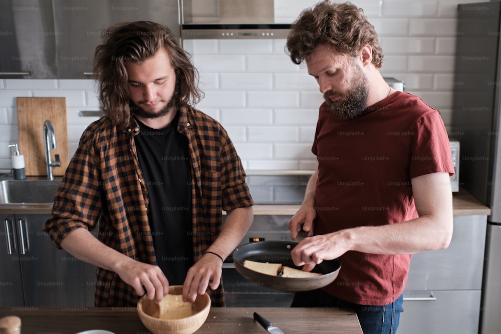 Porträt von zwei Männern, die in der Küche stehen, kochen, Salat machen. Ein Mann steht vor der Kamera, ein anderer dreht ihm den Rücken zu