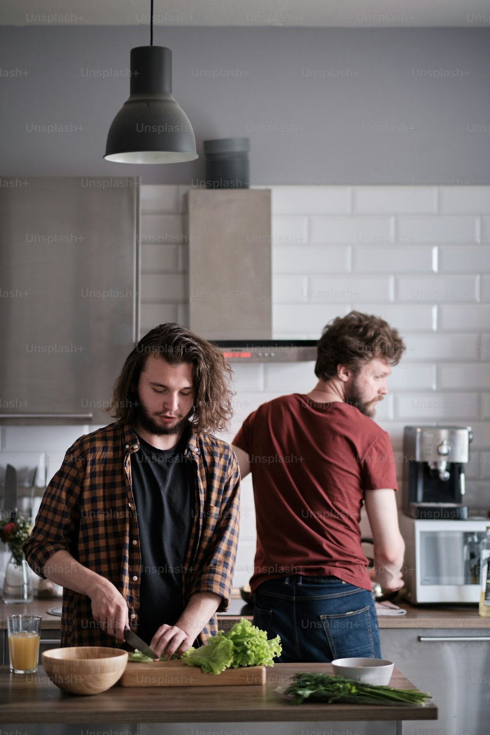 Retrato de dois homens em pé na cozinha, cozinhando, fazendo salada. Um homem está de frente para a câmera, outro virou as costas