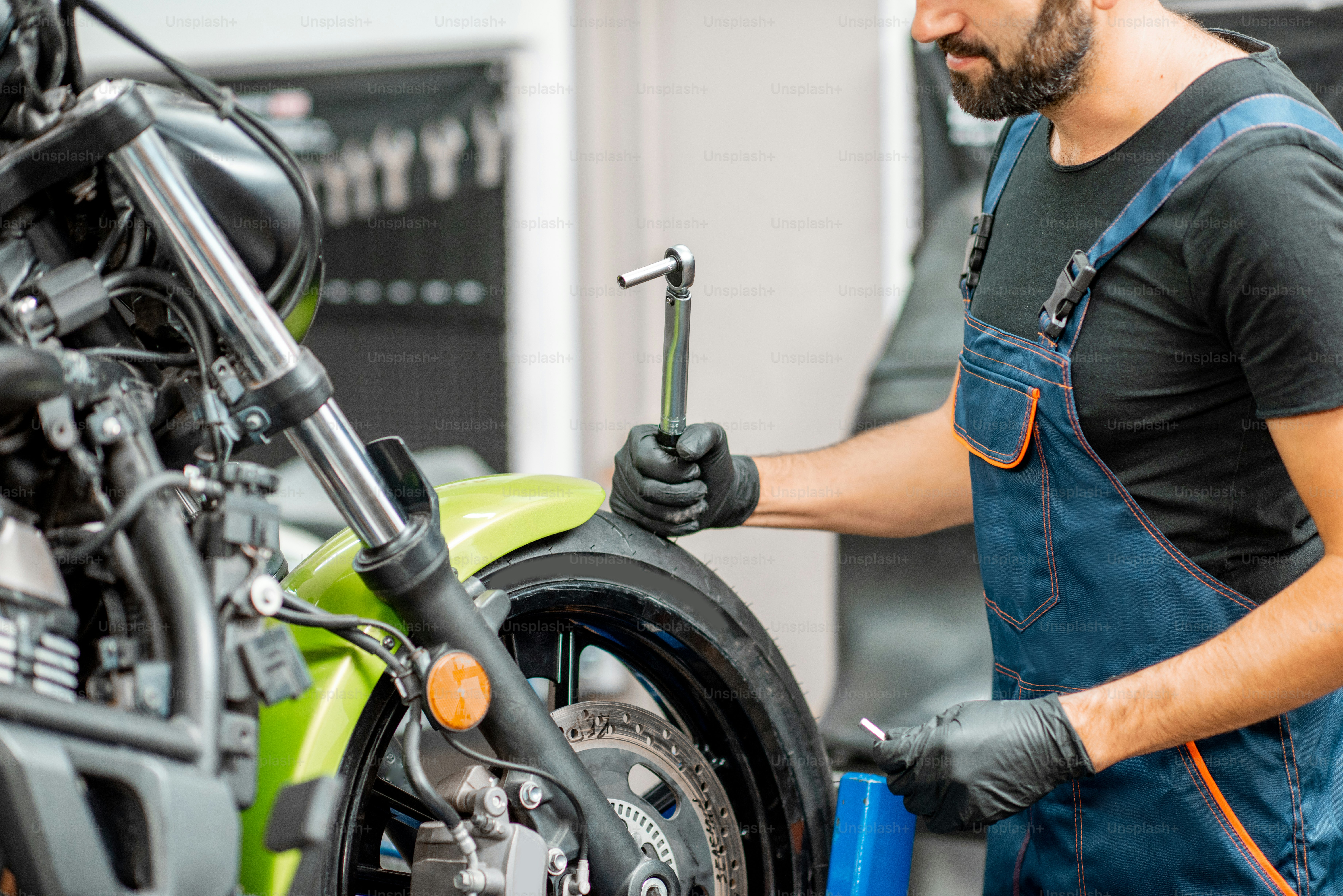 Mechanic in overalls repairing sports motorcycle at the workshop indoors