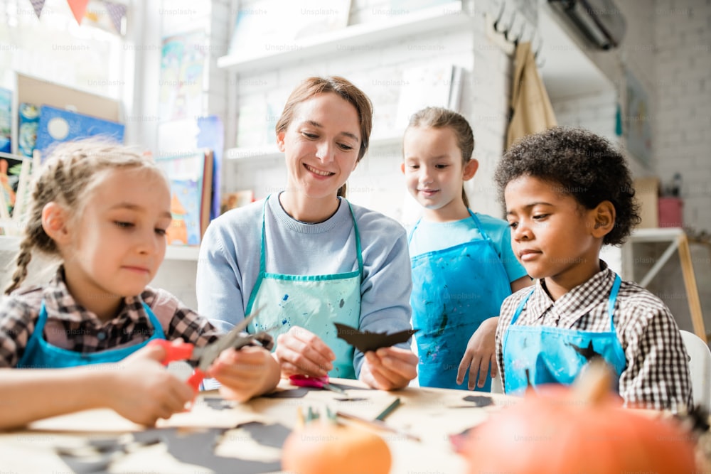 Multicultural youthful schoolkids and their teacher looking at handmade holiday paper decoration at lesson