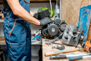 Trabajador desmontando el motor de una motocicleta durante una reparación en la mesa de trabajo del taller, primer plano sin rostro