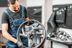 Service worker in working overalls holding motorcycle disk, changing tires in the workshop for motorcycle repairment