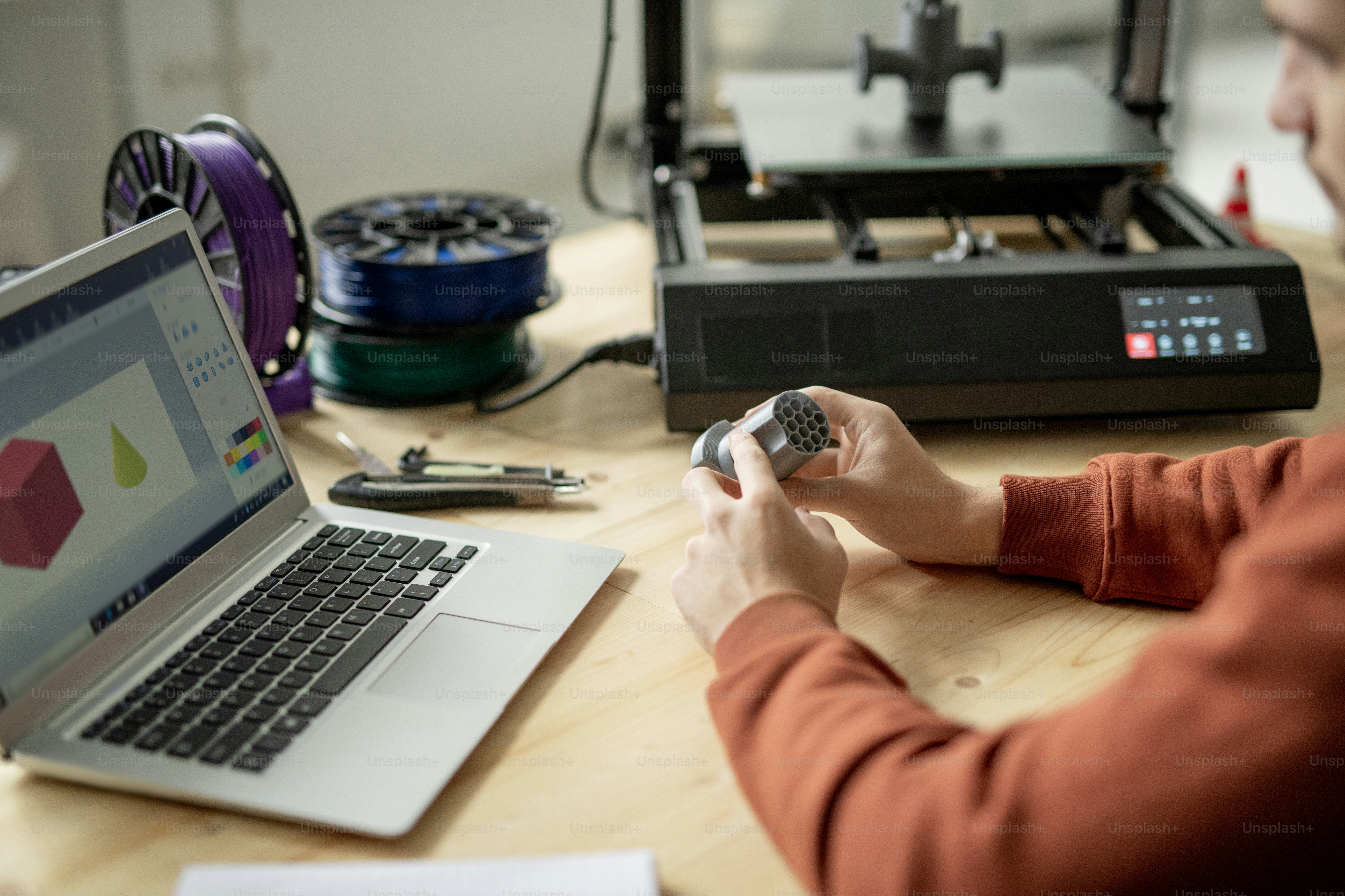 Hands of young male engineer or designer holding geometric figure over wooden table while sitting in front of laptop
