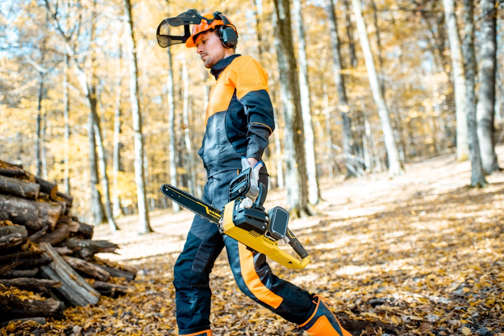 Lifestyle portrait of a professional lumberjack in protective workwear walking with a chainsaw in the forest