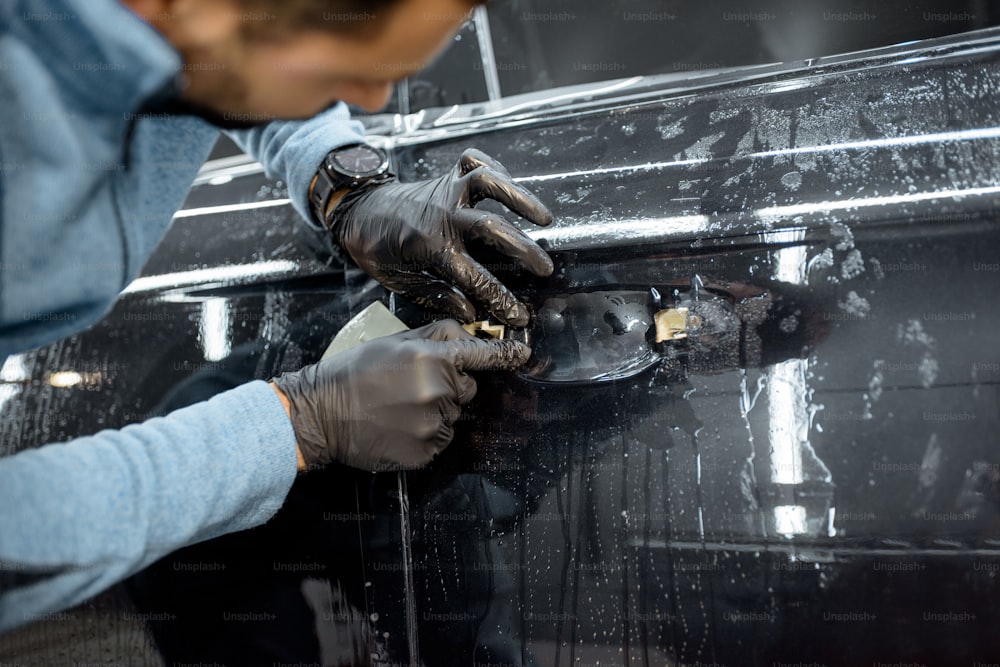 Trabajador pegando una película transparente protectora en la carrocería de un automóvil en lugar de la manija de la puerta, vista de cerca