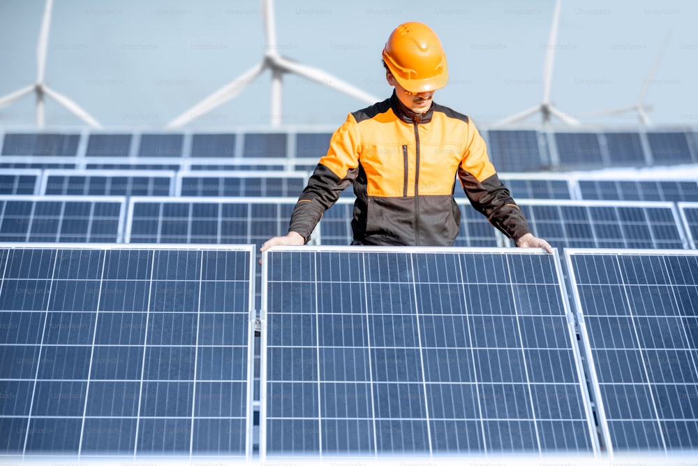 Well-equipped worker in protective orange clothing installing or replacing solar panel on a photovoltaic rooftop plant. Concept of maintenance and installation of solar stations