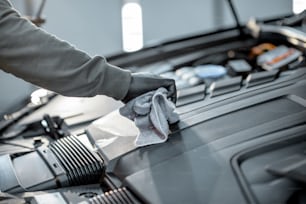 L'uomo esegue una pulizia professionale dell'auto, pulisce il motore con microfibra alla stazione di servizio, vista ravvicinata