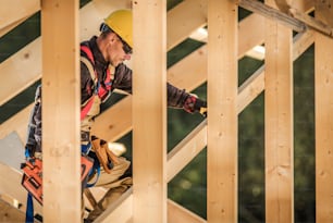 Wood Construction Job. Caucasian Contractor with Nail Gun in Hand Attaching Wood Beams. Industrial Theme.