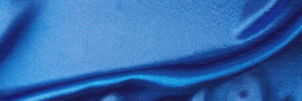 折り目のある青い絹の背景。 波打つサテンの表面の抽象的な質感、長いバナー