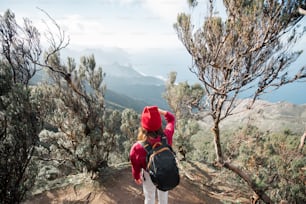 Mulher de chapéu vermelho desfrutando de uma vista deslumbrante sobre a costa rochosa da ilha de Tenerife enquanto viaja altamente nas montanhas da floresta tropical