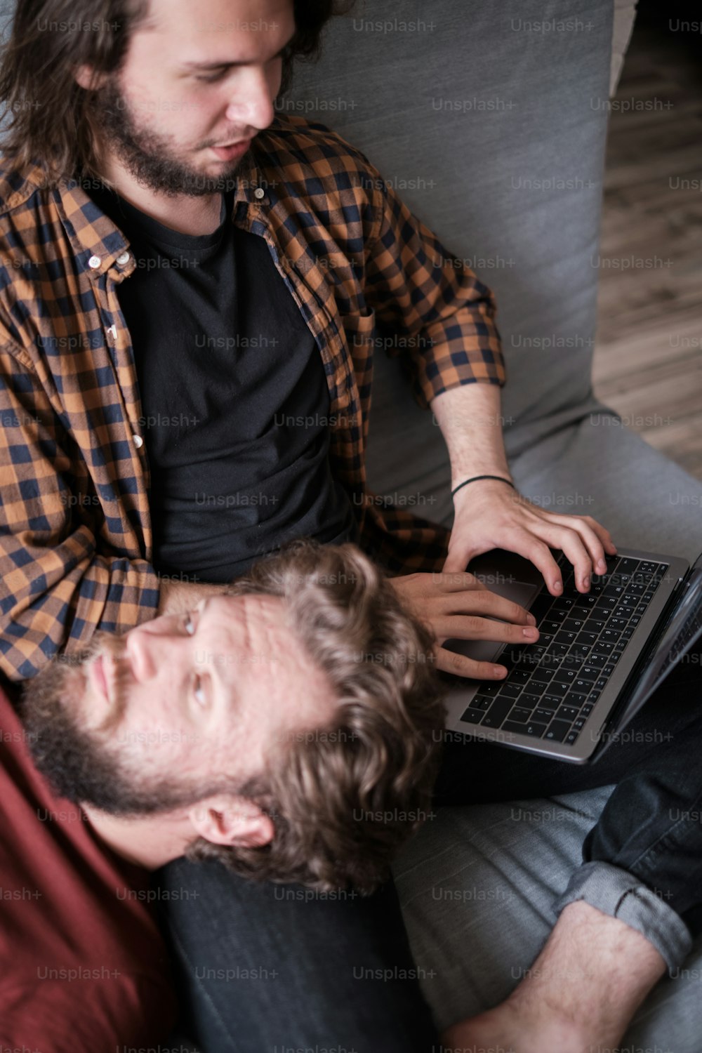 Portrait of two mid age bearded men laying on the sofa, relaxing, spending time together, one is using laptop