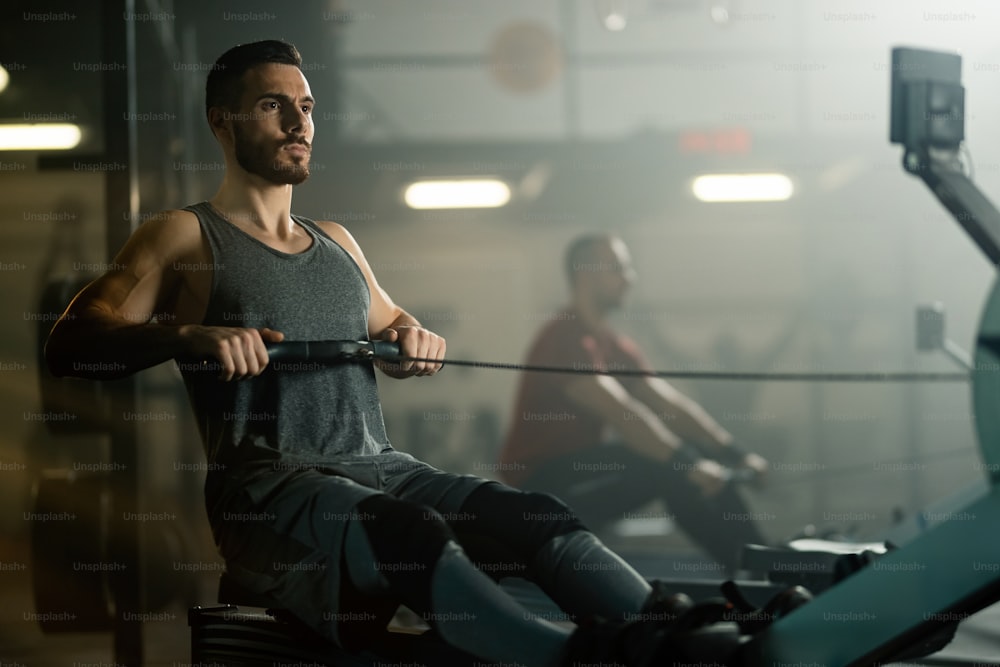 Jovem esportista que se exercita na máquina de remo enquanto se exercita em uma academia.