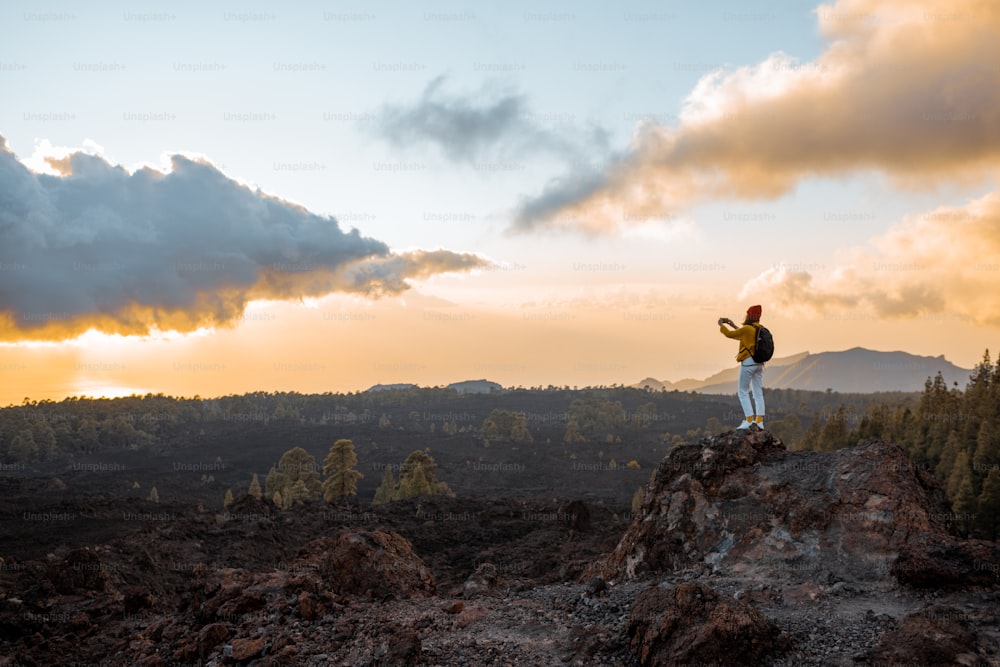 Woman photographing volcanic landscapes on a sunset while standing on the rocky land during the travel