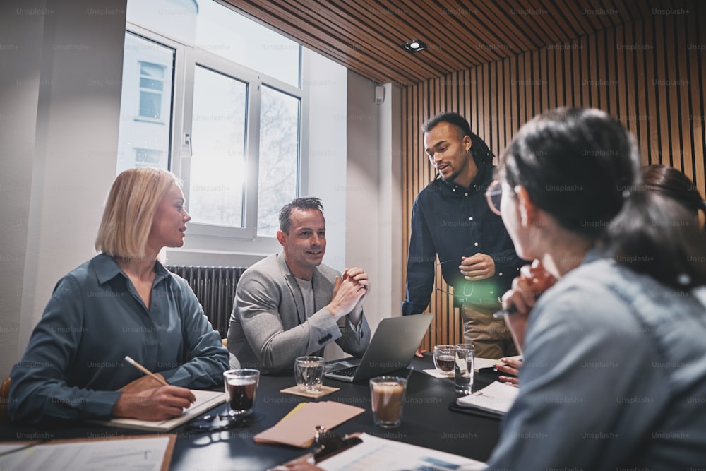 Grupo diverso de empresarios sonrientes hablando juntos durante una reunión con su gerente en una sala de juntas de oficina