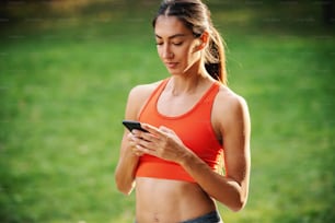 Ritratto di giovane sportiva attraente e magra che si prende una pausa dopo aver corso e utilizzato lo smartphone per inviare messaggi di testo sui social media.
