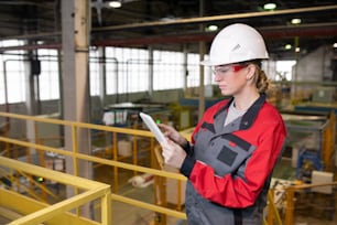 Horizontal medium portrait of female factory engineer in protective workwear using tablet PC