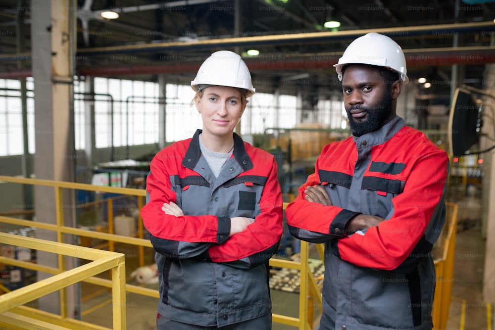 Horizontal medium portrait of two professional factory engineers standing with arms crossed looking at camera