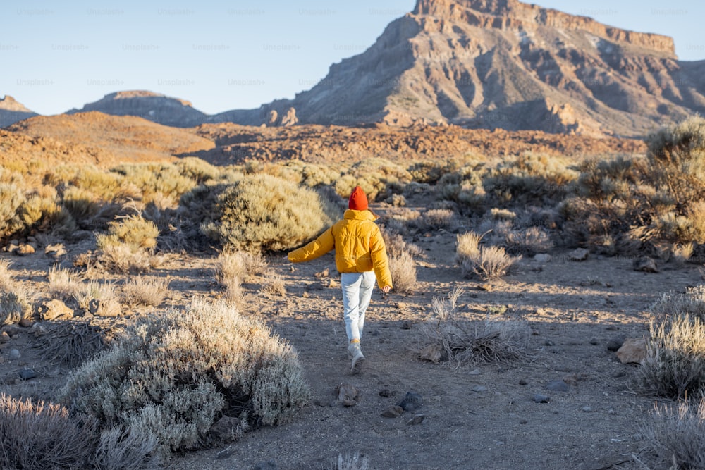 Woman in yellow jacket and red hat on the beautiful volcanic valley with mmountains on the background during a sunset. Traveling on Tenerife island, Spain