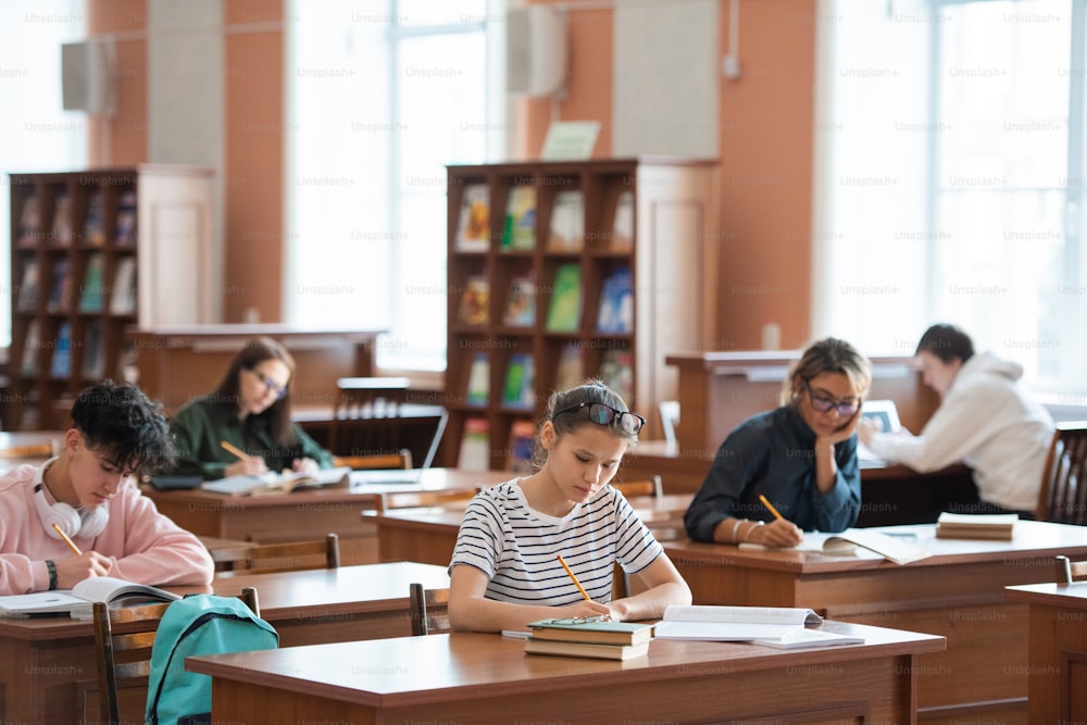Mehrere College-Studenten machen Notizen, während sie am Schreibtisch sitzen und sich auf ein Seminar oder eine Hausaufgabe in der Bibliothek vorbereiten