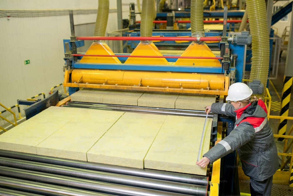 Prise de vue horizontale en grand angle d’un ouvrier d’usine professionnel mesurant la taille de la dalle d’isolation thermique