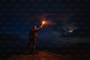 El hombre con un palo de fuegos artificiales parado en la montaña nocturna