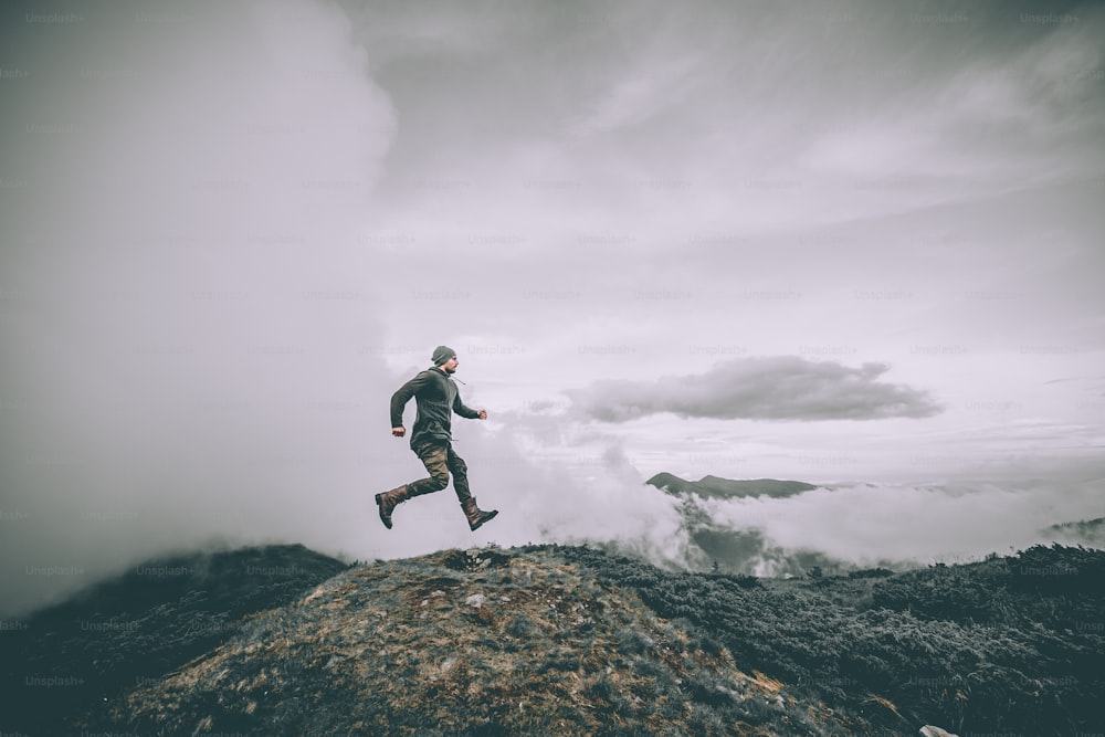 El hombre saltando en la montaña sobre un hermoso fondo de nubes