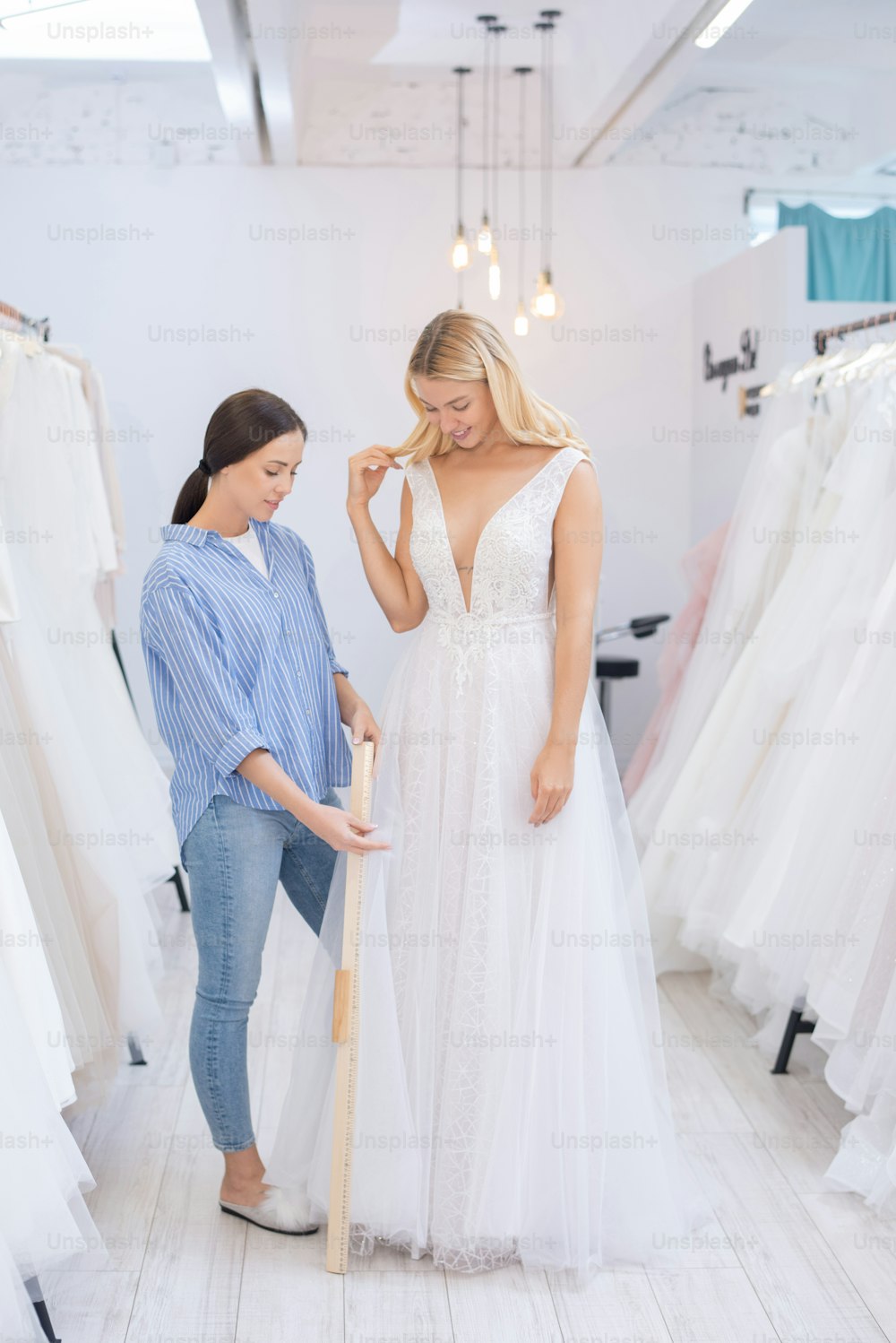 Consultor de vestidos de novia usando regla de madera mientras mide la longitud de la falda de novia en la tienda