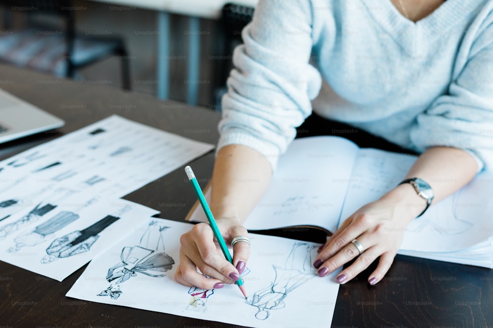 Primer plano de una mujer irreconocible que trabaja en el diseño del boceto de la moda en la mesa