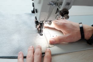 Close-up of unrecognizable male sewer with bracelet sewing zipper to leather fabric under light