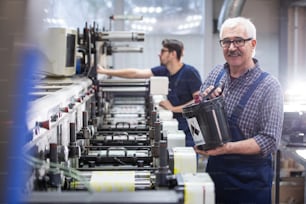 Porträt eines lächelnden älteren Mannes mit Schnurrbart, der Tinte in die industrielle Druckmaschine gießt
