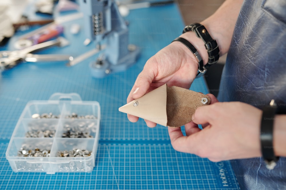 Primo piano dell'operaio irriconoscibile con braccialetti che tengono il prodotto in pelle con bottoni automatici sopra la scrivania con contenitore