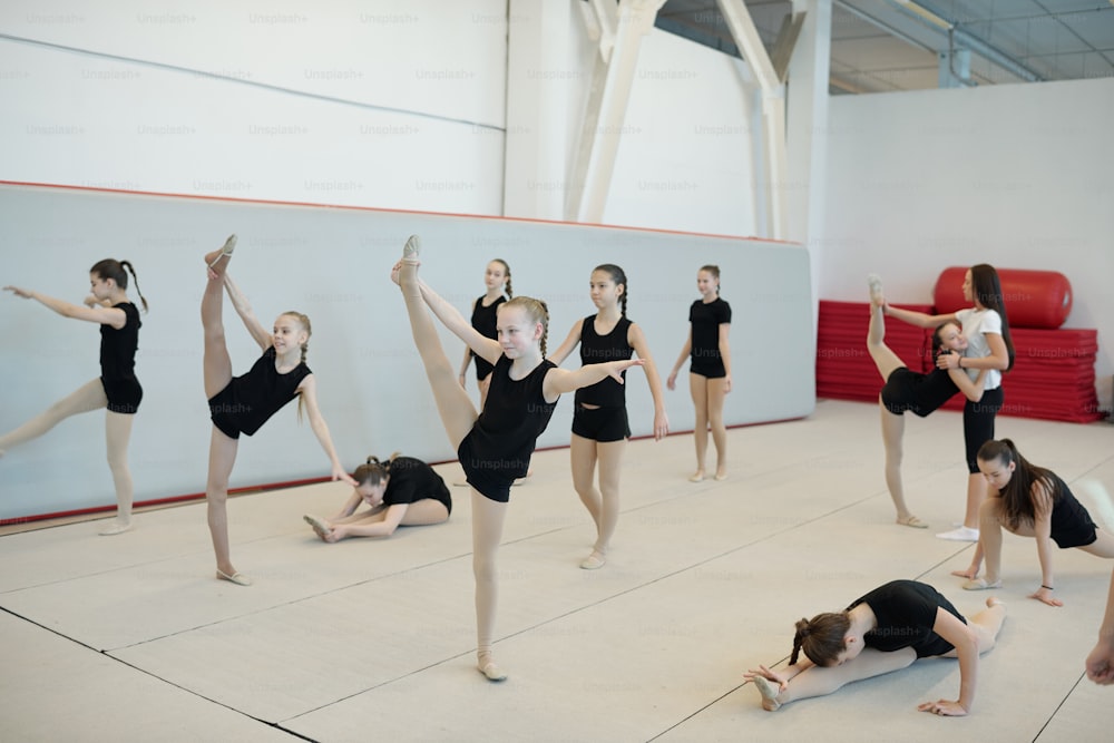 Group of flexible teenage girls doing split or warm-up stretching exercises at cheerleading training