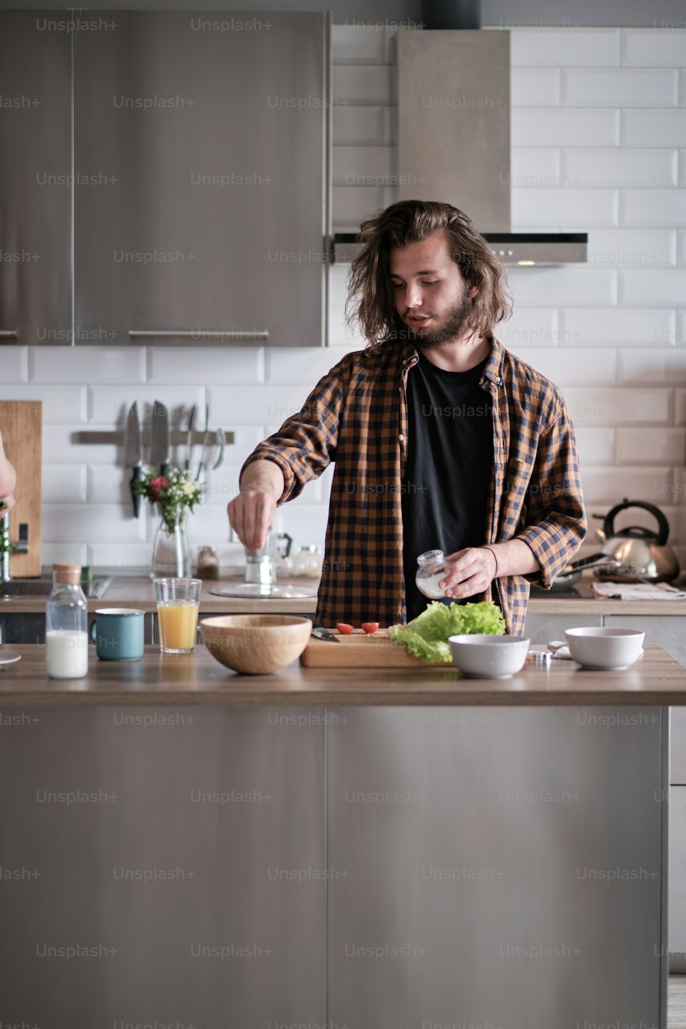 Young man with long hair in brown shirt cooking something in the light kitchen