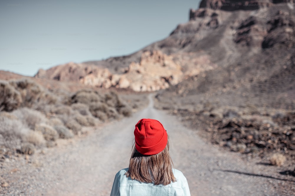 Ritratto di stile di vita di una donna spensierata vestita casualmente in jeans e cappello rosso che si gode il viaggio sulla valle deserta, vista posteriore