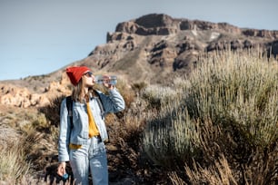 Young woman in red hat traveling with backpack on the volcano valley, feeling thirst and drinking water