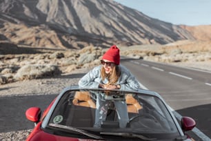 Lifestyle portrait of a young woman enjoying road trip on the desert valley, getting out of the convertible car on the roadside