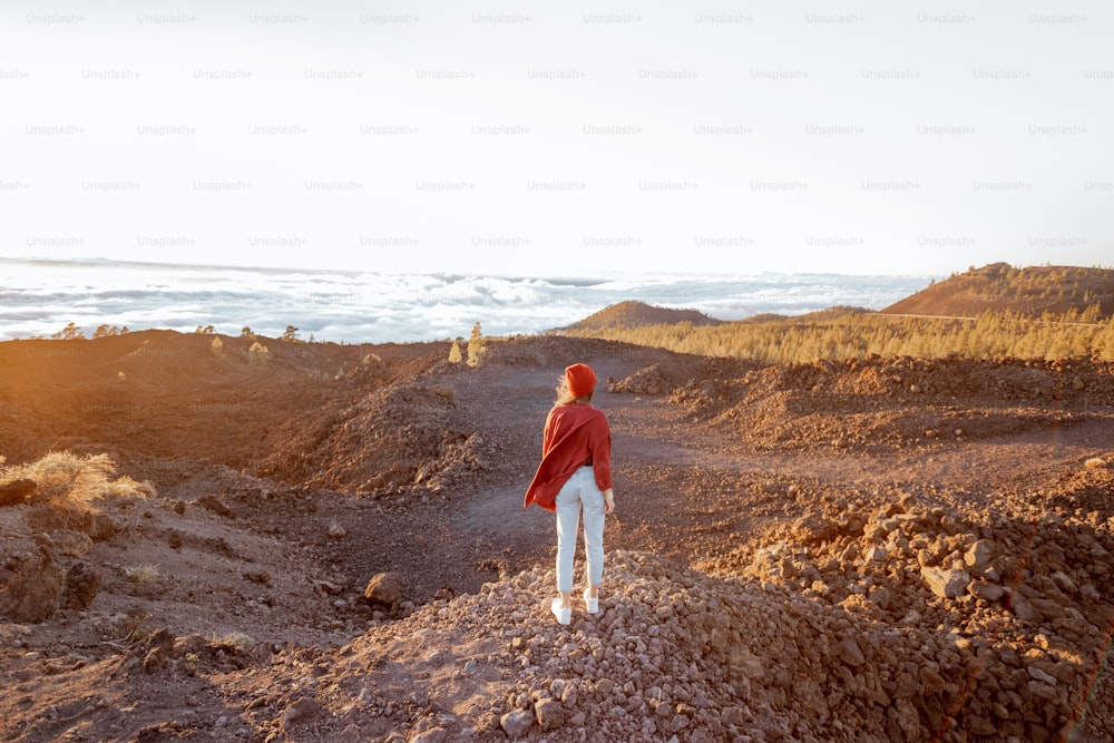 Woman walking on the rocky terrain above the clouds, enjoying beautiful sunset while travel