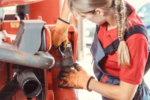 Woman machinist working with wrench of a farm machine doing some fixing or maintenance